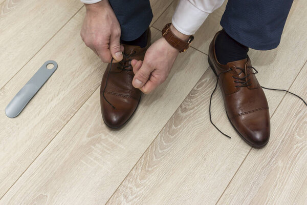 Hands of man in suit pants tying laces on classic shoes in everyday lifestyle