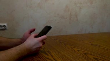 Masada oturan adamın elleri akıllı bir telefonu kaydırıyor.