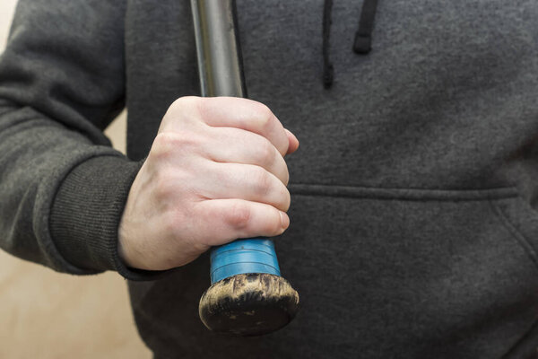 Hand in hoodie grips the shabby hilt of a black wooden baseball bat