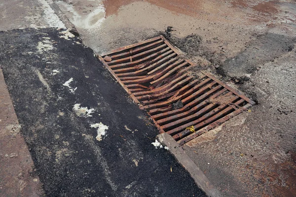 Büyük şehrin çirkin asfalt ve su birikintileri ortasında yağmur sırasında yolda kirli ve paslı Kanal ızgarası — Stok fotoğraf