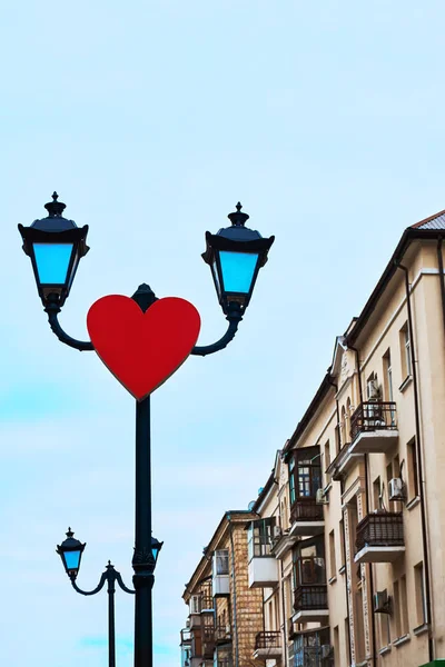 Corazón rojo en un poste de luz por encima del camino en la ciudad — Foto de Stock
