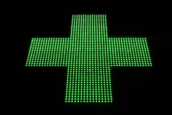 Green LED cross pharmacy and hospital hanging on the street is isolated in black