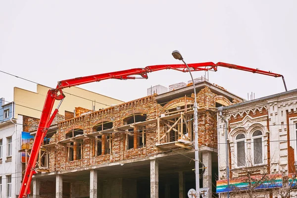 La grande mano rossa di una pompa di calcestruzzo lavora alla costruzione di un nuovo edificio — Foto Stock