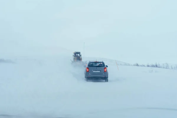 Териберка, Мурманская область / Россия - февраль 2018: Автомобили в снежную бурю едут по проселочной дороге за дорожной техникой по белой пустыне — стоковое фото