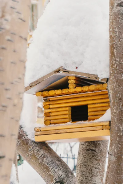 Alimentatore per uccelli in legno da piccoli tronchi di colore marrone chiaro tra gli alberi sotto la neve — Foto Stock