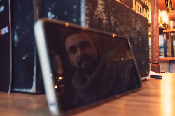 Un joven con barba se refleja en el brillante reflejo de un teléfono inteligente de pantalla grande — Foto de Stock