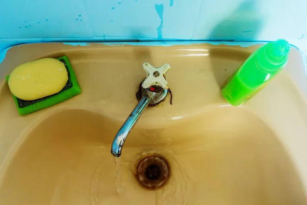 Bir eski, tedavi edilmemiş banyo bir paslı lavabo ve bir sızdıran musluk ve mavi fayans duvar
