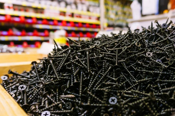 Schwarze Schrauben von selbstschneidenden Schrauben unterschiedlicher Größe werden gegossen und liegen in einer Holzkiste in einem großen Baumarkt vor den Augen aller — Stockfoto