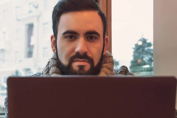 Un bărbat cu barbă lucrează la un proiect serios în spatele unui laptop într-o cafenea confortabilă. — Fotografie, imagine de stoc