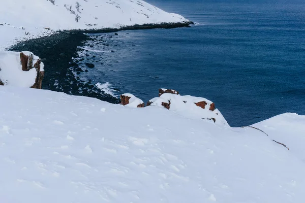 雪の中の下の北の海の海岸にオレンジ色の深刻で危険な岩 — ストック写真