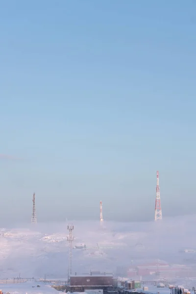 Torres vermelhas e brancas para televisão e comunicações sobressaem das colinas nevadas nos arredores da vila do norte atrás da guarda polar em um dia gelado de inverno — Fotografia de Stock
