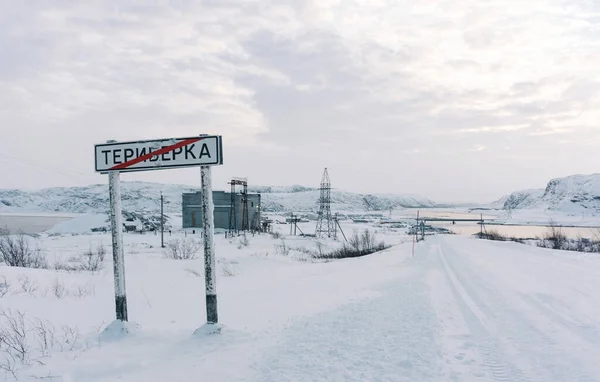 Teriberka, região de Murmansk / Rússia - Fevereiro 2018: Um sinal de estrada avisa para entrar na aldeia de Teriberka em severas geadas de inverno sob neve branca decorada com vários adesivos de turistas Fotografia De Stock
