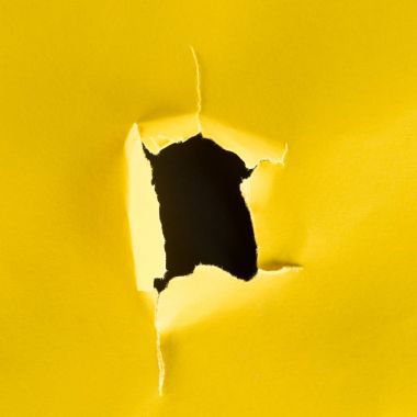 close-up shot of hole in yellow paper isolated on black clipart