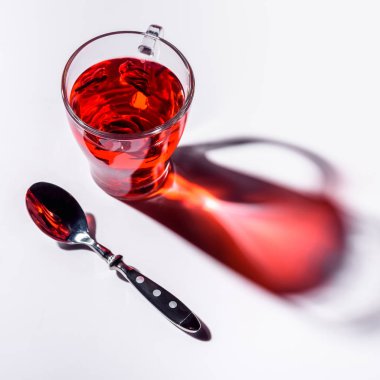 high angle view of glass cup with hibiscus tea and spoon on white table clipart