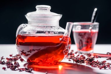 glass teapot with hibiscus tea and cup with spoon on table clipart