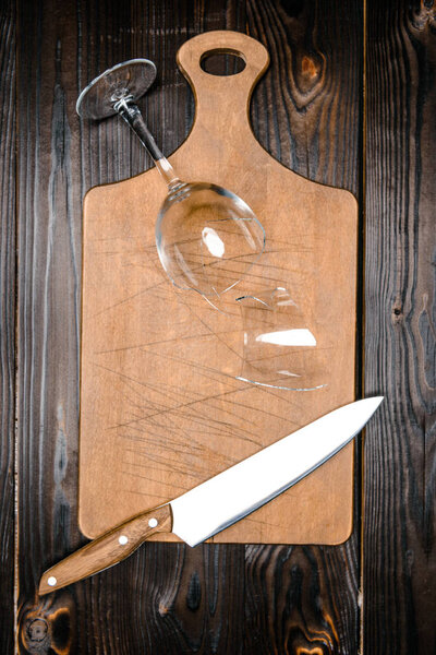 top view of broken wineglass and knife with wooden board on table