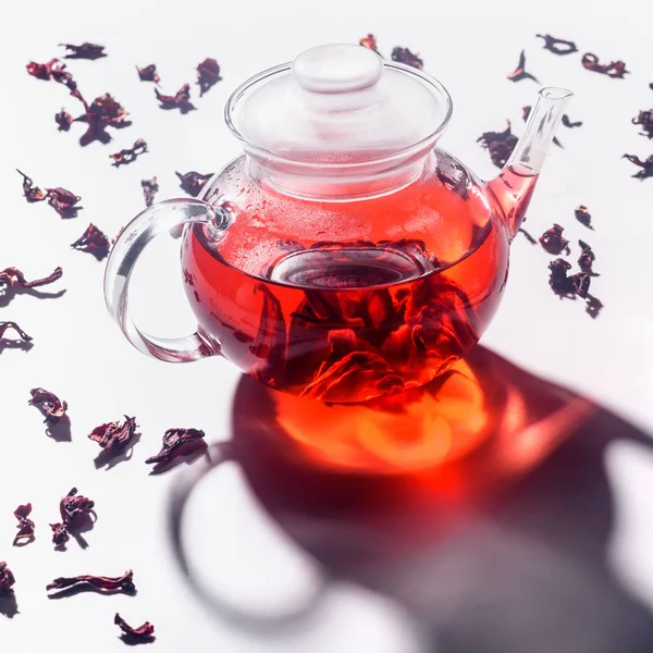 transparent glass teapot with hibiscus tea and scattered tea on table