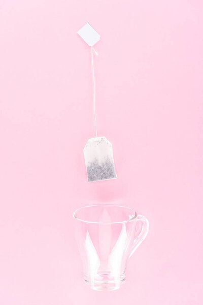 вид сверху на один пакетик чая и пустой стакан стакана изолированы на розовый
