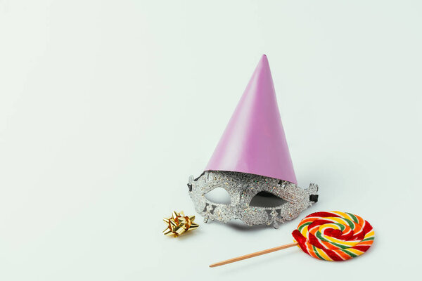 close up view of masquerade mask, party cone and lollipop isolated on grey