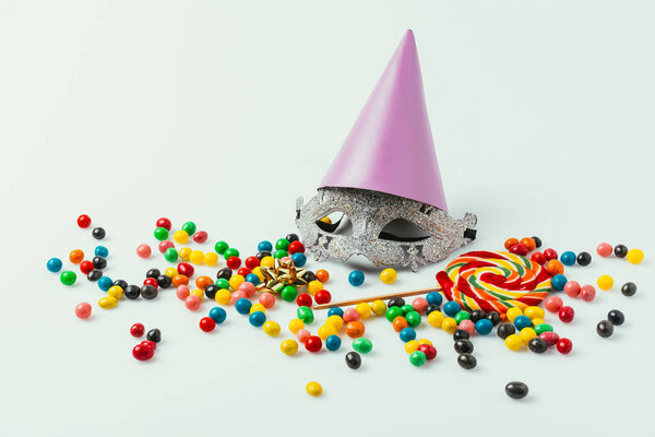 close up view of masquerade mask, party cone and sweets isolated on grey  