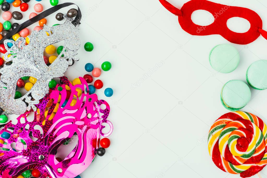 top view of arranged masquerade masks, macarons and candies isolated on grey, purim holiday concept