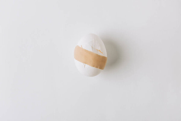 broken white egg with medical plaster laying on white background