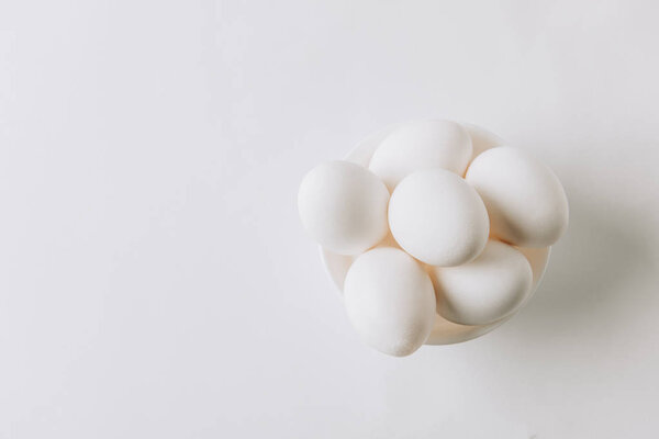 top view of white eggs laying on white plate on white background 