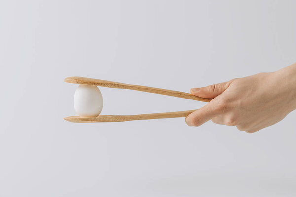 cropped image  of hand holding wooden tongs with white egg 