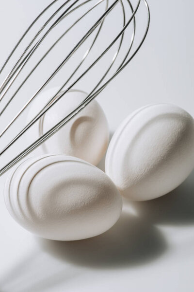 white eggs laying under whisk on white background