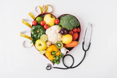 vegetables and fruits laying in heart shaped dish near stethoscope and measuring tape isolated on white background    clipart