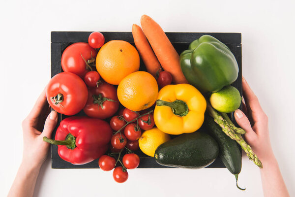 Hands holding vegetables and fruits in dark wooden box isolated on white background