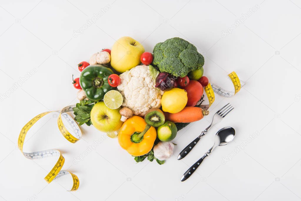 vegetables and fruits laying on white background with fork, spoon and measuring tape  