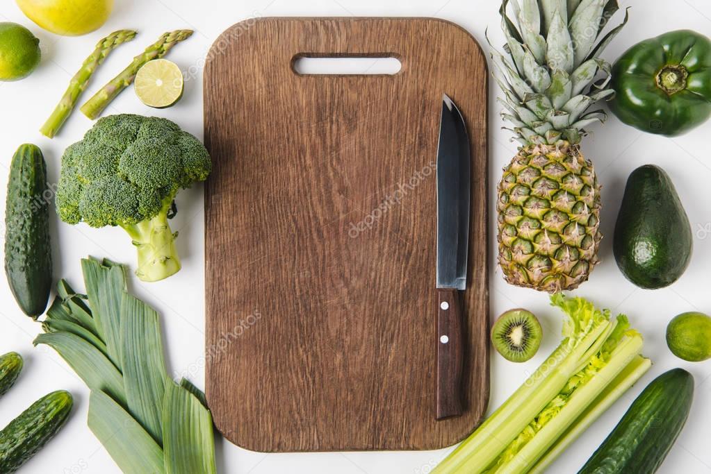 Knife on wooden cutting board with green vegetables and fruits isolated on white background