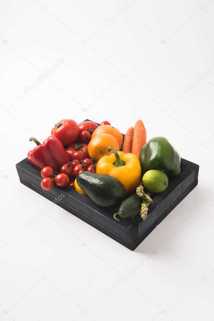 Juicy raw vegetables and fruits in dark wooden box isolated on white background