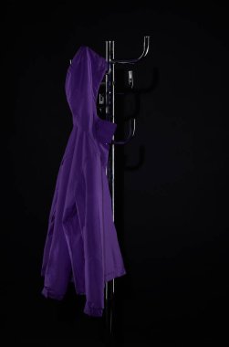 purple raincoat hanging on coat rack isolated on black clipart