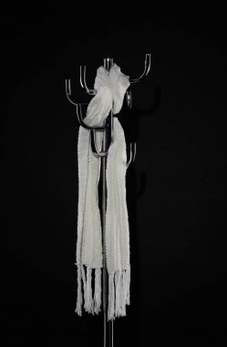 white scarf hanging on coat rack isolated on black clipart