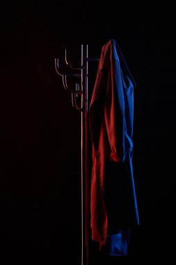 coat hanging on coat rack under toned light isolated on black clipart