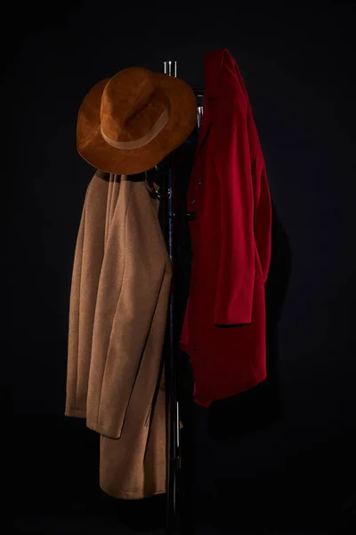 coats and hat hanging on coat rack isolated on black