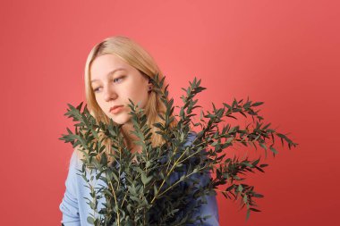thoughtful young woman with bunch of eucalyptus branches isolated on red clipart