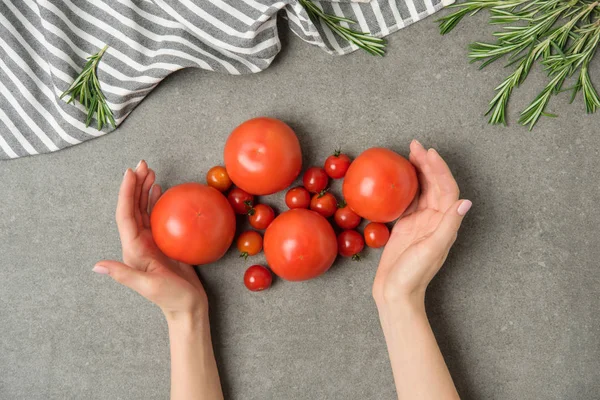 用亚麻和迷迭香将成熟西红柿放在灰色混凝土表面的女性手裁剪镜头 — 图库照片