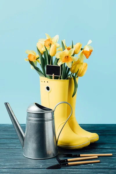 ブルー木製表面に黄色の花束花の水まき缶とガーデニングの長靴で空の黒板のビューをクローズ アップ — ストック写真