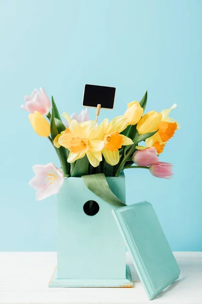 青に分離された木製のテーブルの上の巣箱に空の黒板と花の美しい花束のビューをクローズ アップ — ストック写真