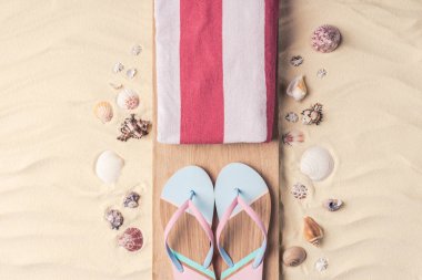 Flip flops and towel with shells on light sand clipart