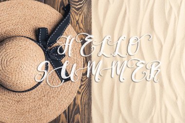 Straw hat on wooden pier on sandy beach with hello summer inscription clipart