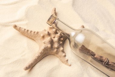 Starfish and bottle with letter on light sand clipart