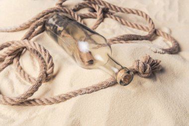 Corked bottle with message and rope on sandy beach clipart