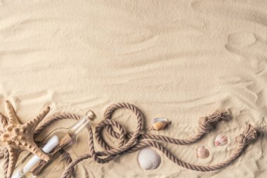 Bottle with letter and shells with rope on light sand clipart