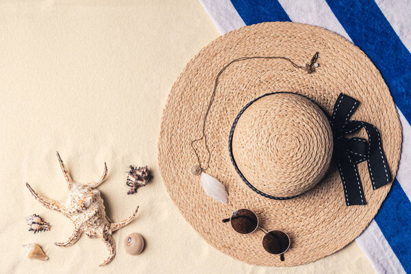 Straw hat with sunglasses and seashells on sandy beach