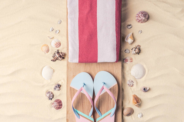 Flip flops and towel with shells on light sand