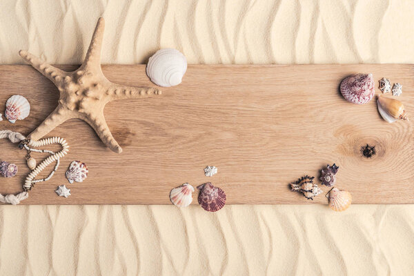 Summer travel template with seashells on wooden pier on light sand